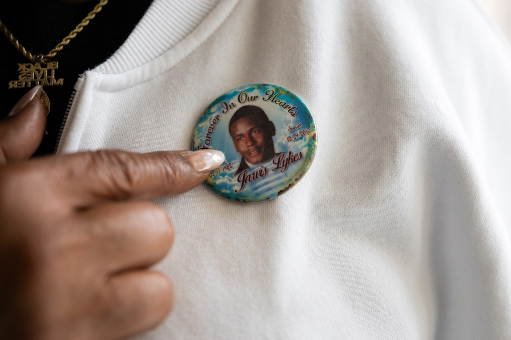 A closeup on a woman's finger pointing at a button with a young man on it.