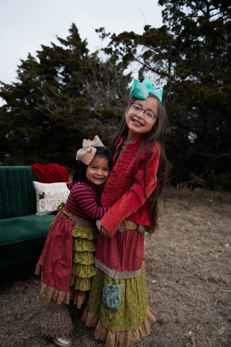 Tow young girls embrace and smile at the camera.