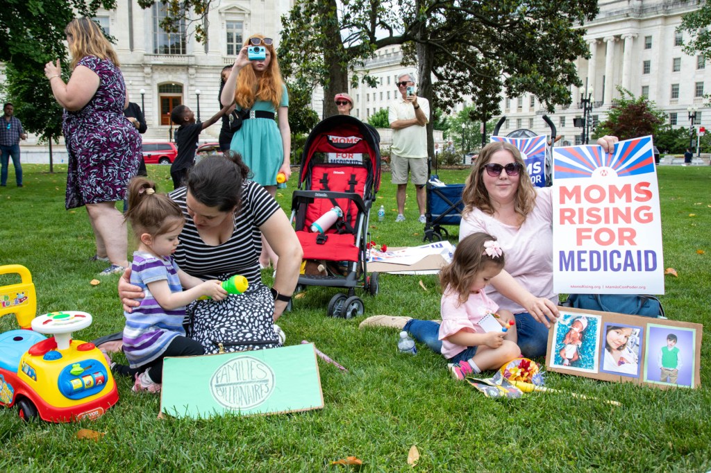 Mothers with young children sit on the grass outside the U.S. Capitol protesting cuts to Medicaid.
