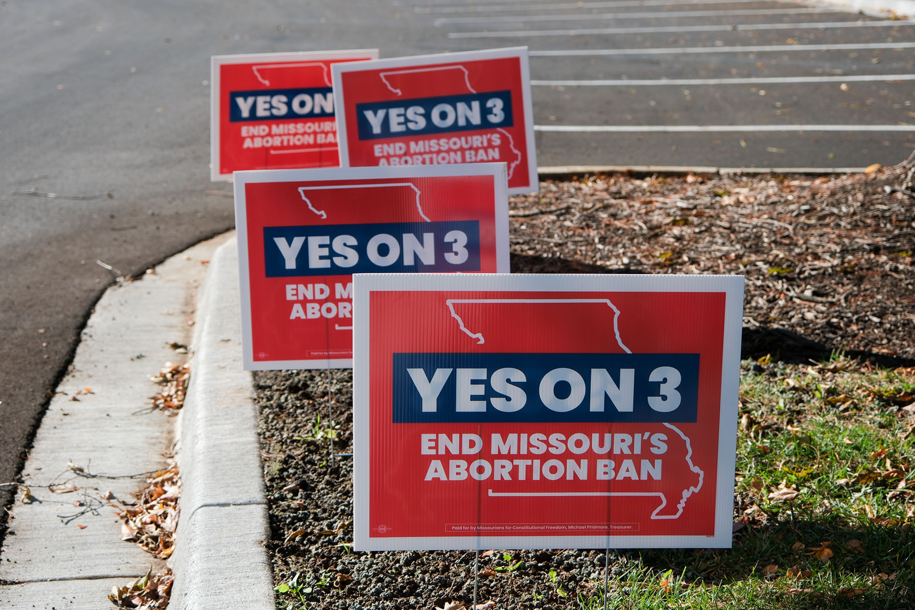 Red and blue yard signs reading “Yes on 3 – End Missouri’s Abortion Ban” are posted along the edge of a parking lot.