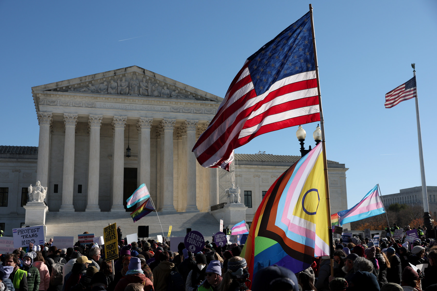 A crowd waves transgender and LGTBQ+ flags in front of the Supreme Court.