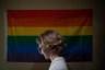 A young trans person in front of a rainbow flag.