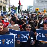 Protesters hold signs and sunflowers in Los Angeles amid ICE raids.