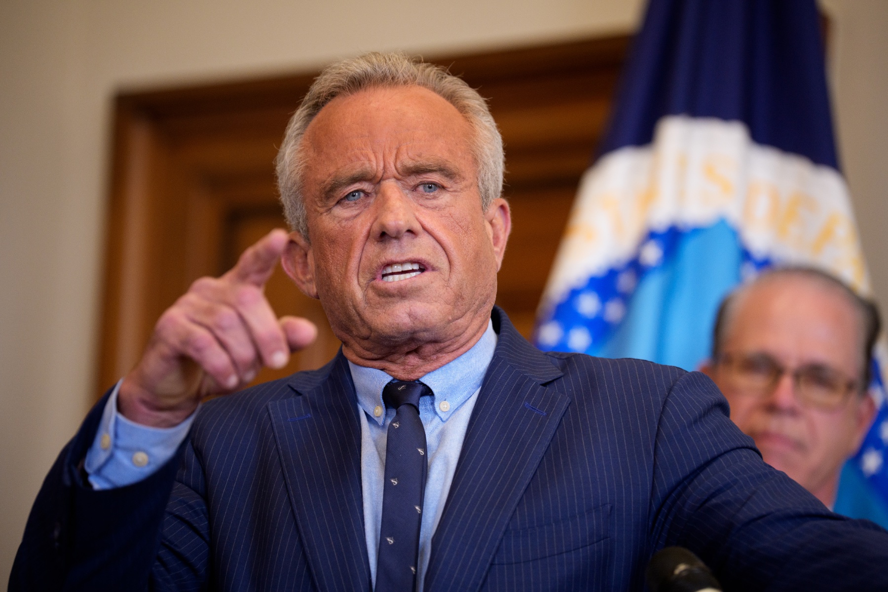 Health and Human Services Secretary Robert F. Kennedy Jr. speaks while pointing his finger wearing a blue suit with stripes on it.