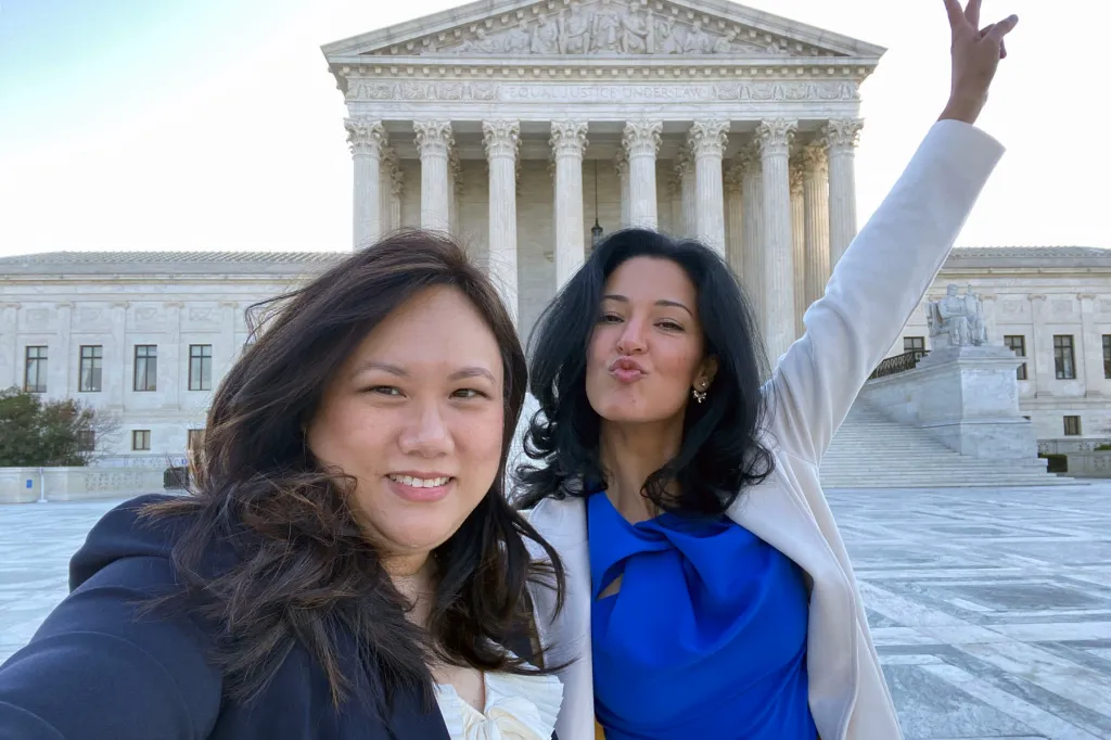 Narkis Golan poses smiling with her lawyer Karen King in front of the U.S. Supreme Court, where grand white columns rise behind them. Golan raises her arm in a peace sign.