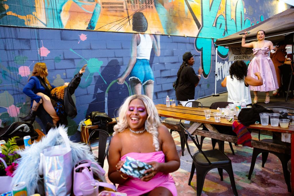Several partygoers laugh and dance against a colorful mural backdrop.