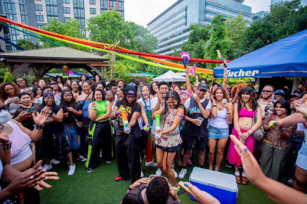 A group of people surround two people shooting water guns at someone.
