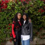 Mother and daughter stand in front of a wall of flowers.