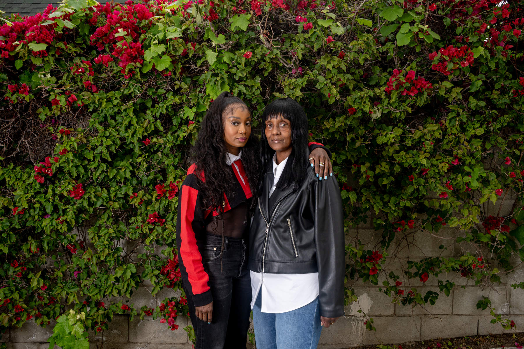 Mother and daughter stand in front of a wall of flowers.