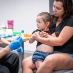 A mother holds her child while she gets vaccinated.
