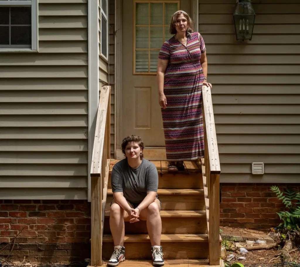 A person sits at the bottom of outside stairs, with another person standing at the top of them.