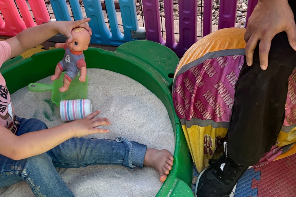 A child plays with a doll in a sandbox.