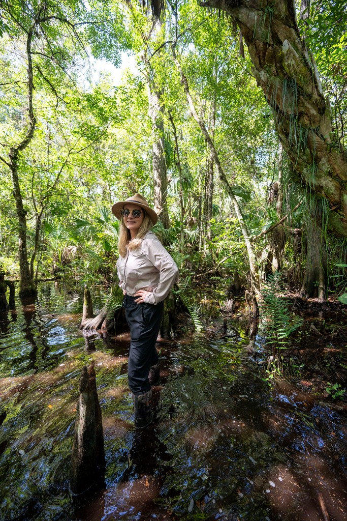 A woman stands knee deep in water surrounded by trees.