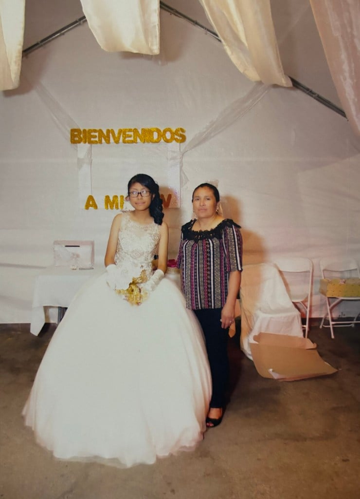 Estela Ramos stands next to a girl in a quinceañera dress under a decorated tent. The photo was taken before her deportation.
