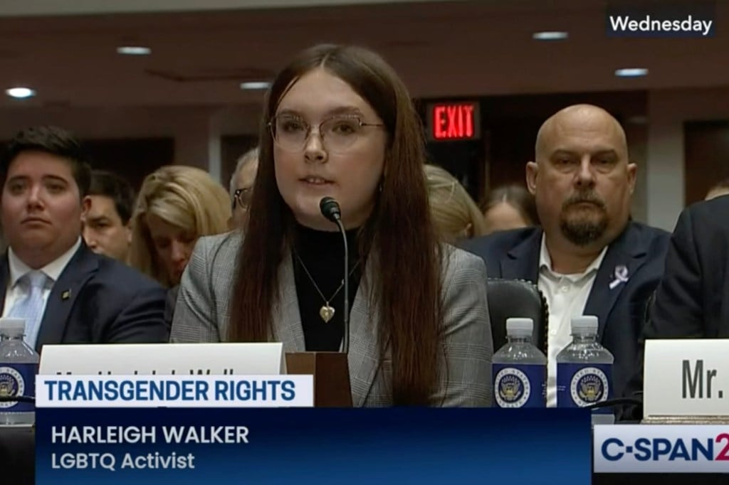 A screenshot of C-SPAN2 footage of Harleigh Walker sitting at a lectern with a microphone in front of her. Her father is sitting behind her. The chyron reads: Transgender rights; Harleigh Walker, LGBTQ Activist.