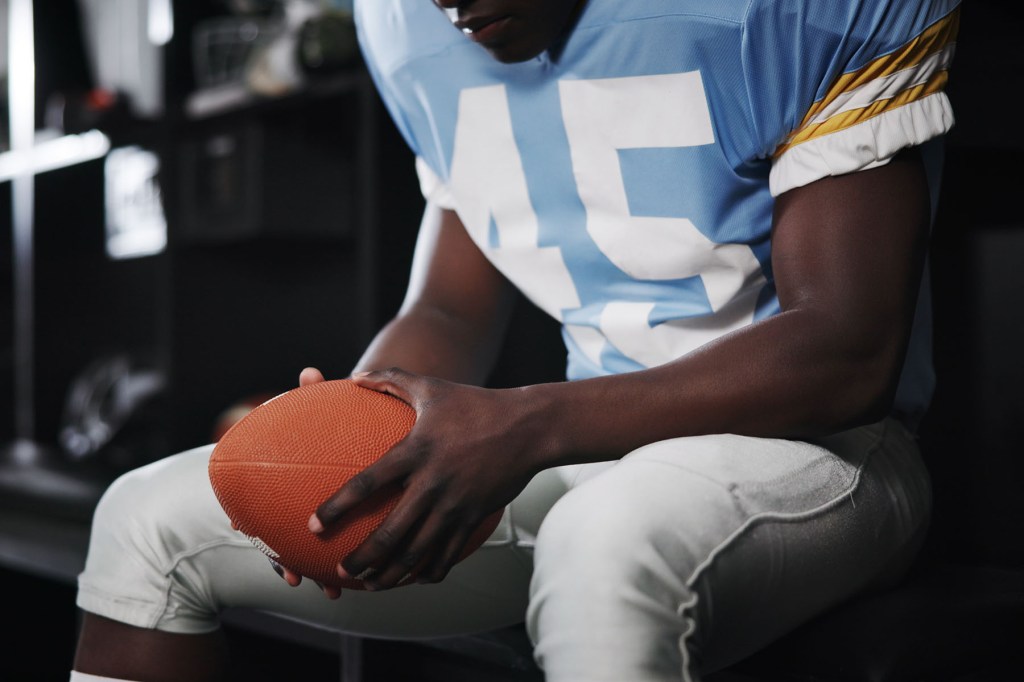 A player with a ball his hand sits in a locker room.