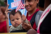 A woman holds a baby who holds an American flag.