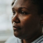 A black woman stares into the distance with a strong expression on her face.
