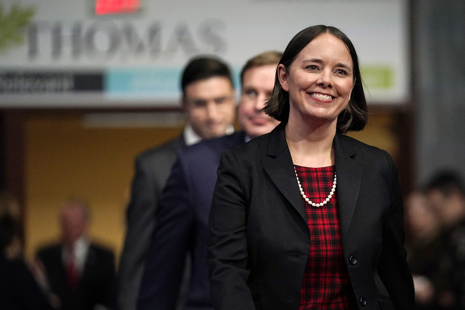 Shenna Bellows smiles, walking down a hallway surrounded by men in suits and military uniforms.