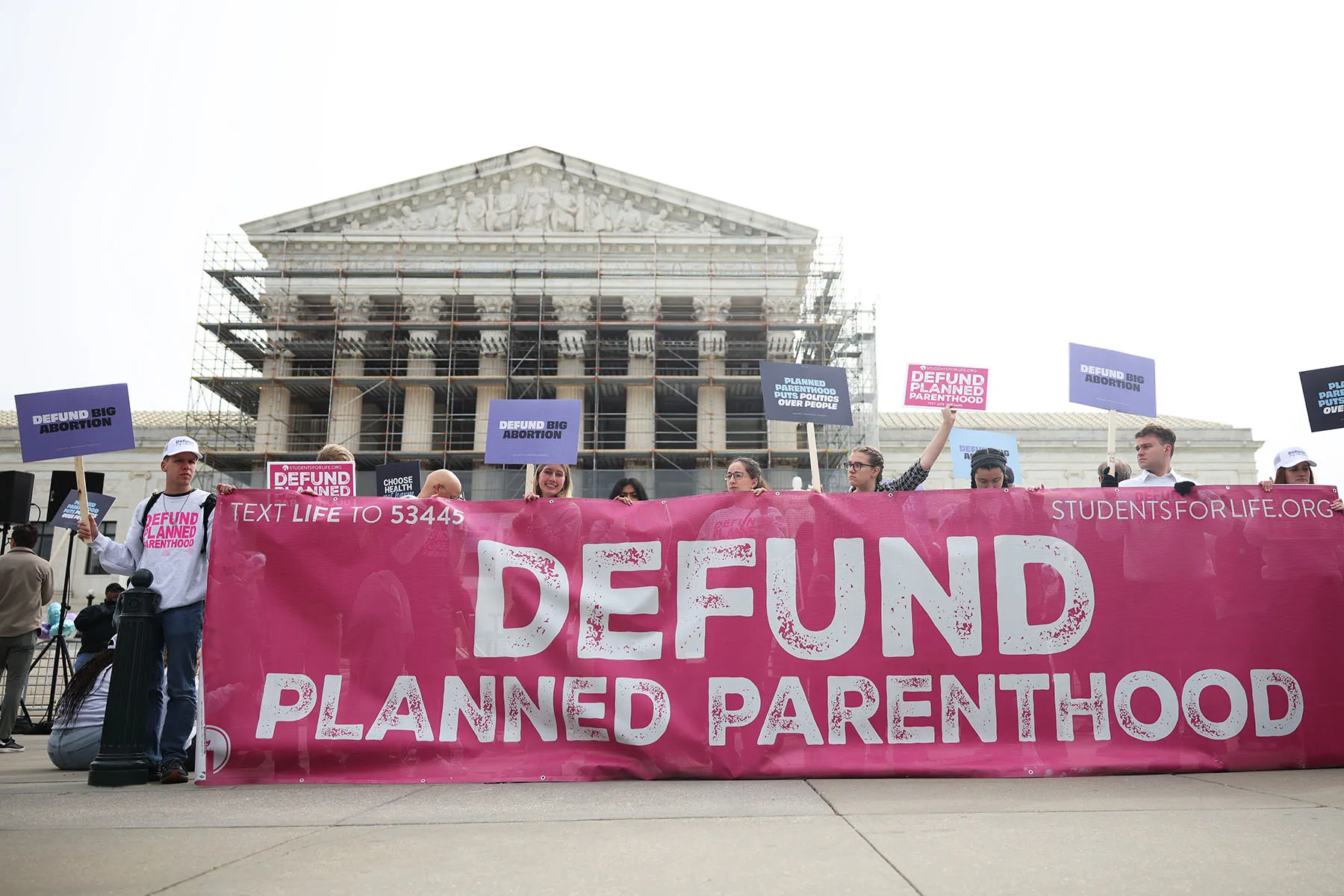 Anti-abortion protestors gather outside the Supreme Court holding a banner that reads "Defund Planned Parenthood"