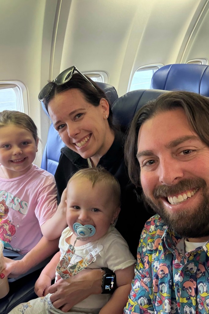 A mother, father and two children smile at the camera while on a flight.