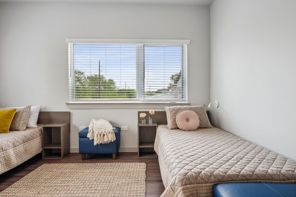 A bedroom with two twin beds, simple modern furniture, and a window.