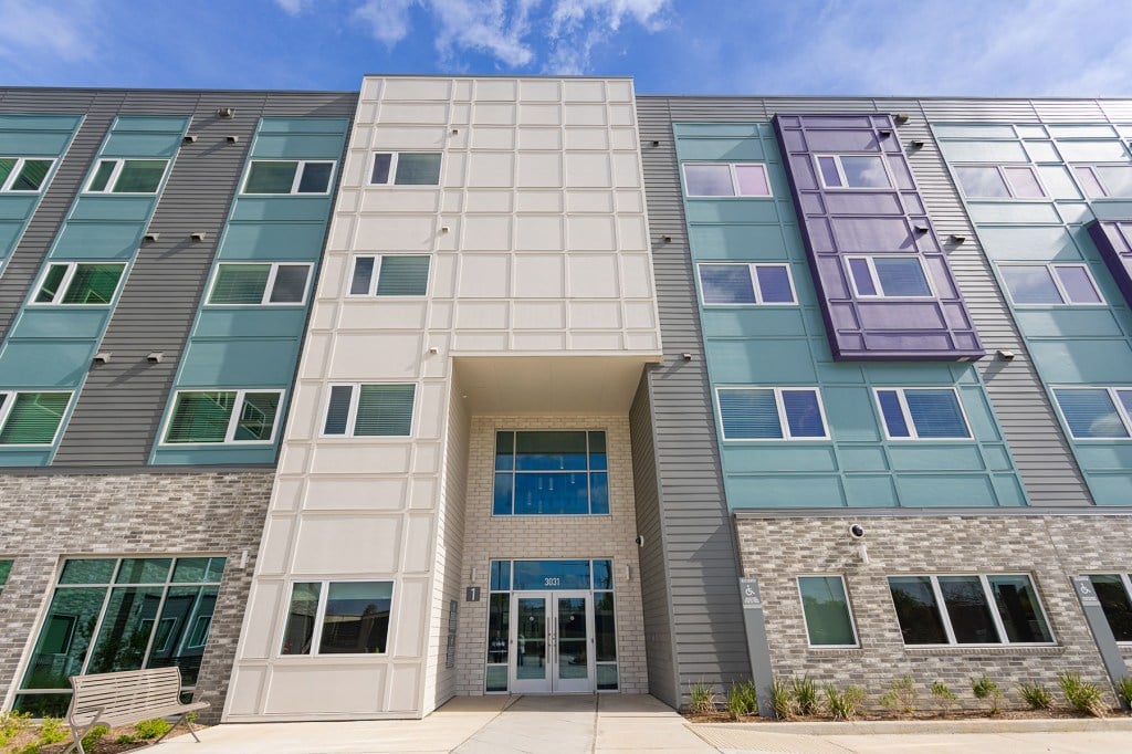 A modern, multi-story residential building with teal, gray, and white siding and large windows.
