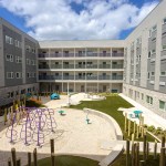 A courtyard surrounded by apartment buildings, with a playground, climbing structure, and green space.