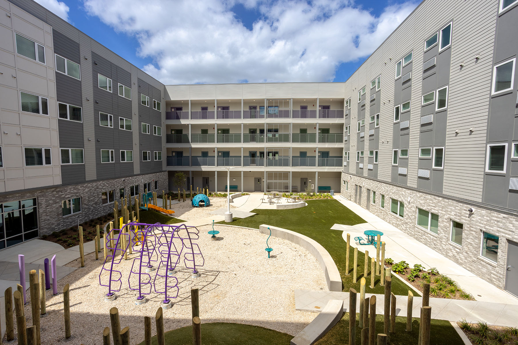 A courtyard surrounded by apartment buildings, with a playground, climbing structure, and green space.