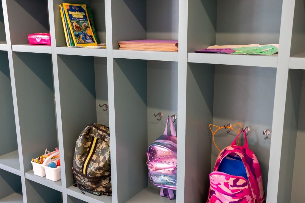 A row of gray cubbies with children’s backpacks and books inside the family area of One Safe Place.
