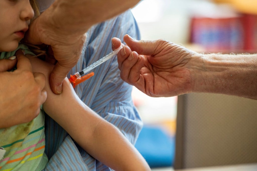 A young child receives a vaccine in their arm while being held by an adult.