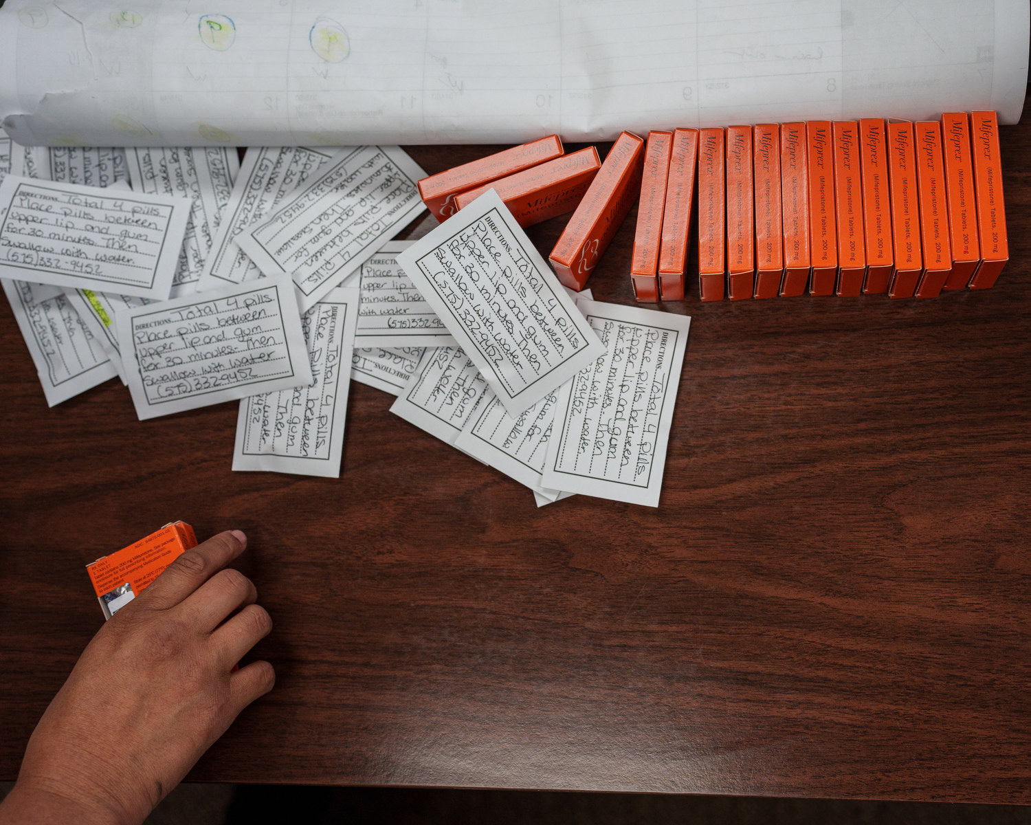 A hand reaches into frame on a table with several boxes and papers with medical instructions.