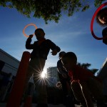 Children play at a playground silhouetted against the sun above them.