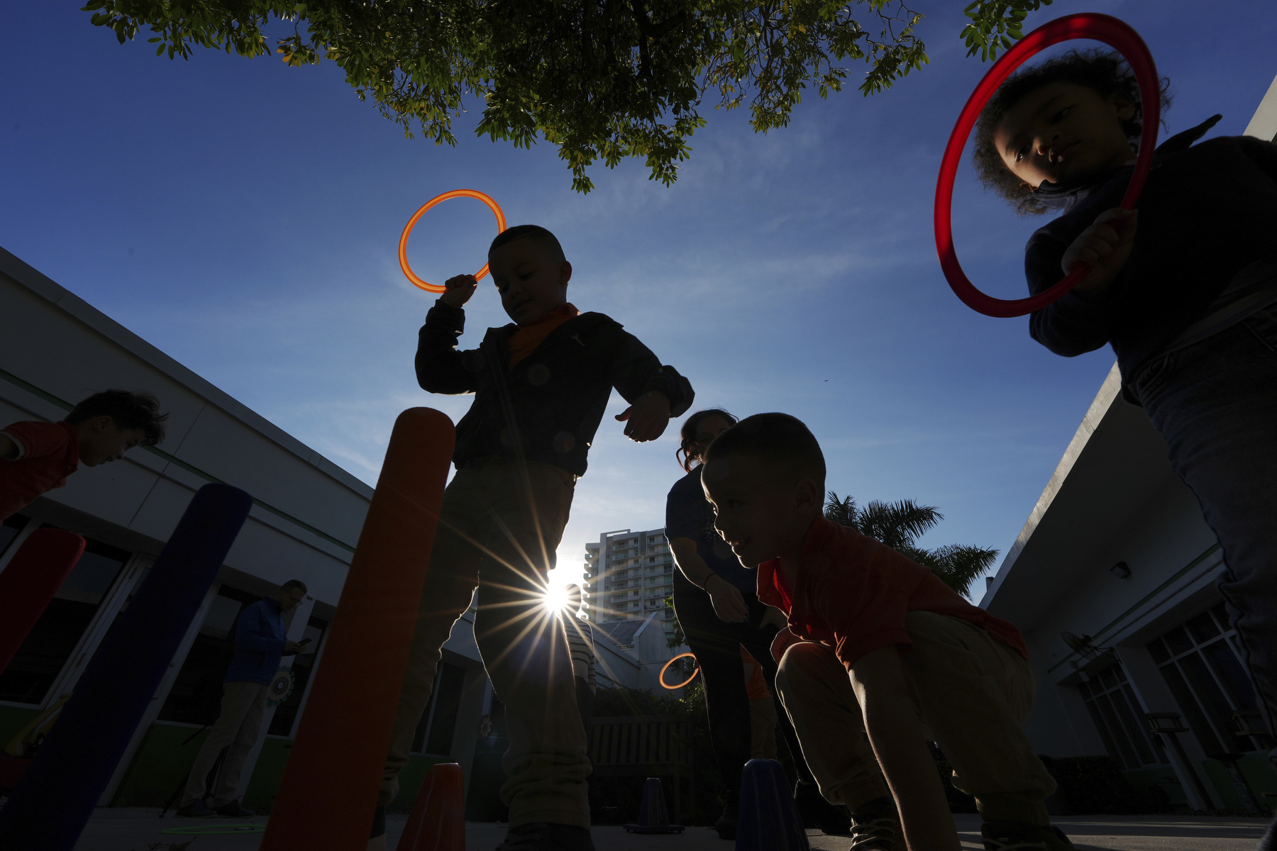 Children play at a playground silhouetted against the sun above them.