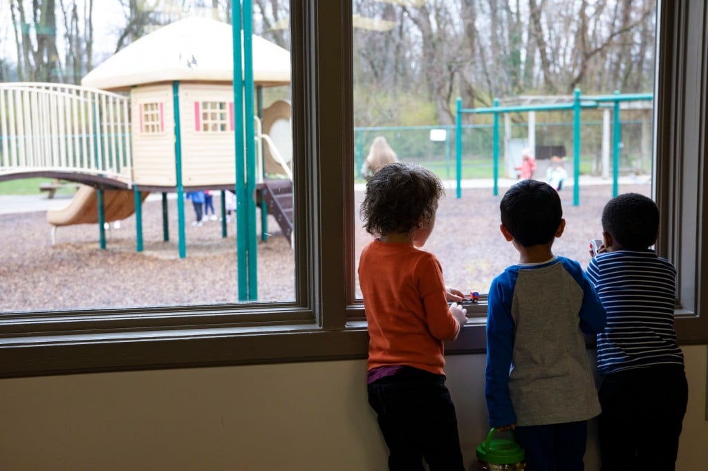 Three children look out the window of a childcare facility.