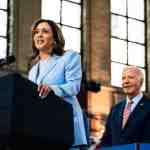 Kamala Harris stands at a podium with Biden standing behind her.