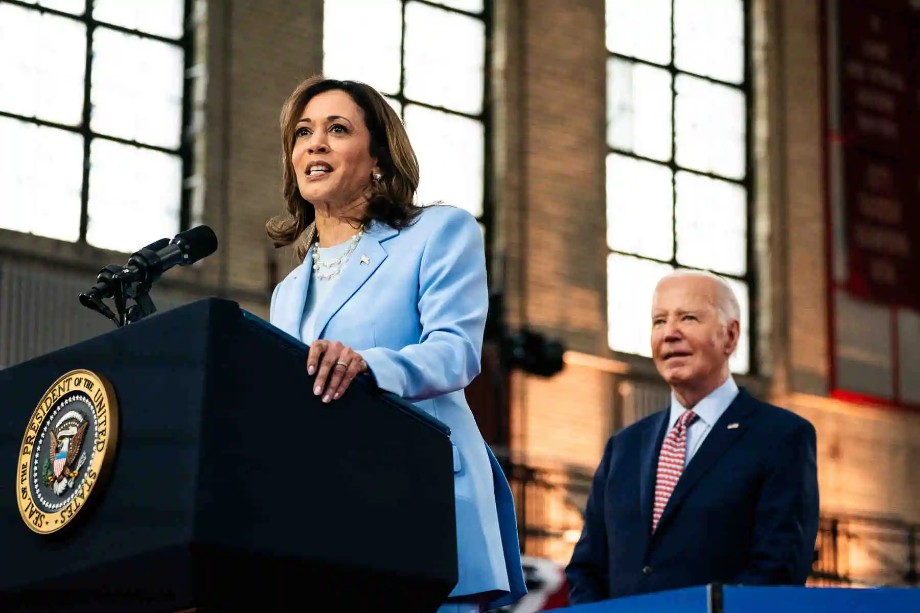 Kamala Harris stands at a podium with Biden standing behind her.