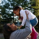 A mother playfully lifts her young daughter up in the air.