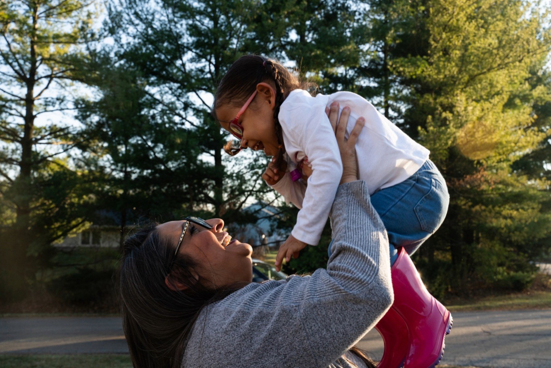 A mother playfully lifts her young daughter up in the air.