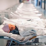 A newborn baby boy sleeps in an infant bed in a hospital hallway.