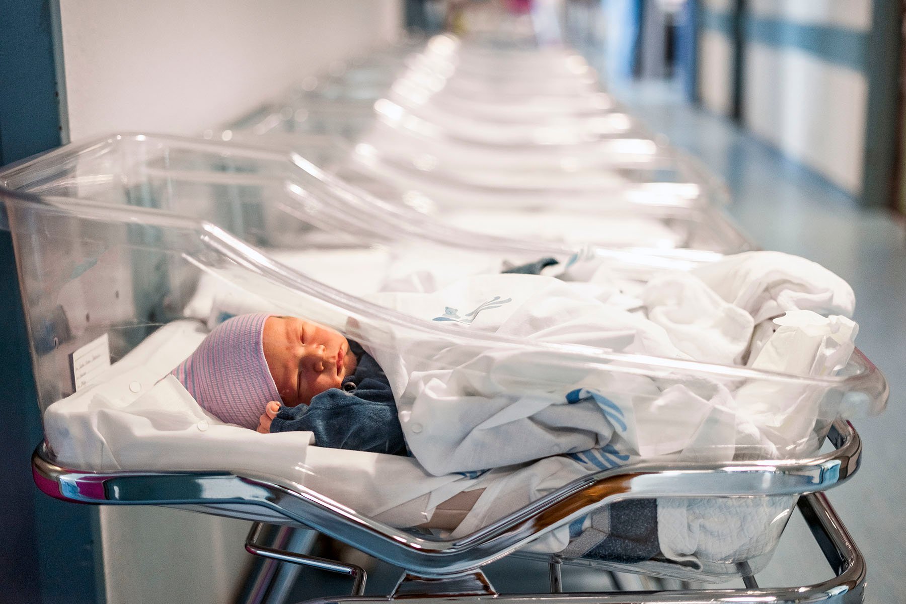 A newborn baby boy sleeps in an infant bed in a hospital hallway.