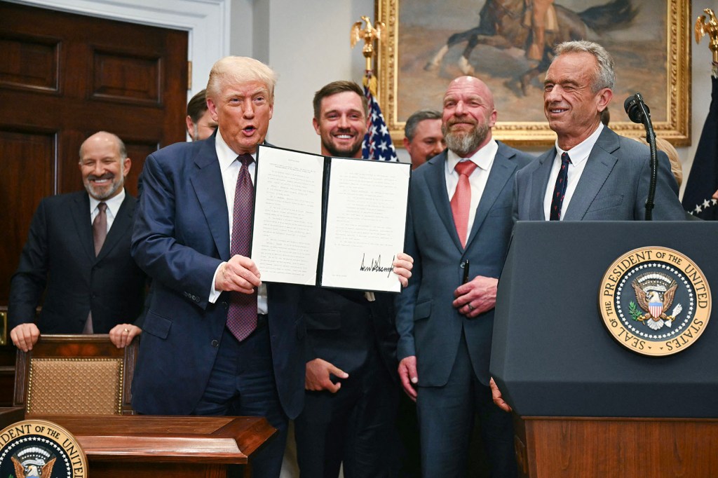 President Donald Trump stands, flanked by Secretary of Commerce Howard Lutnick, golfer Bryson DeChambeau, WWE CCO Triple H and Secretary of Health and Human Services Robert F. Kennedy Jr., after signing an executive order restarting the Presidential Fitness Test.