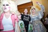 A group of activists, including two drag queens, chant and raise their fists outside a bathroom at the Texas Capitol. A person in a “Trans Texas” T-shirt and others hold signs reading “Bathroom Bigot!!” with a caricature of a lawmaker.