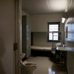 A shadow is cast on the wall outside an empty prison cell