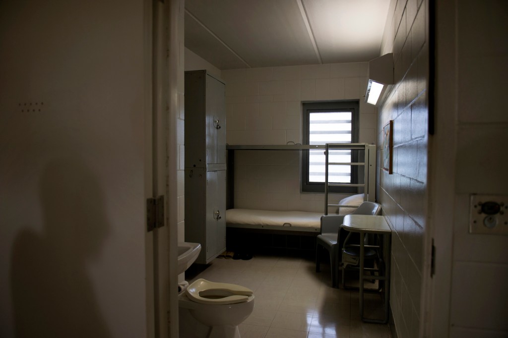 A shadow is cast on the wall outside an empty prison cell