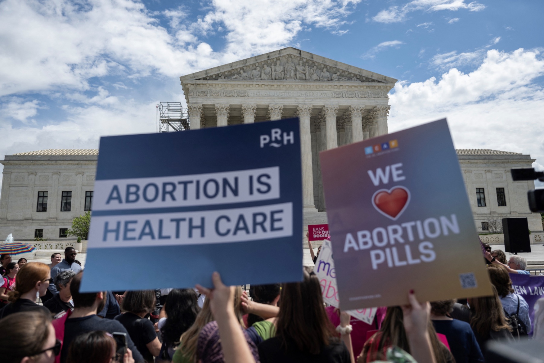 Signs that say "Abortion is health care" and "We heart abortion pills" are held in front of the Supreme Court building.