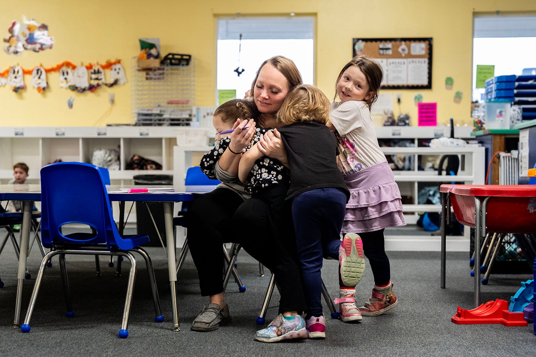 Toddlers give their teacher a hug in a classroom.