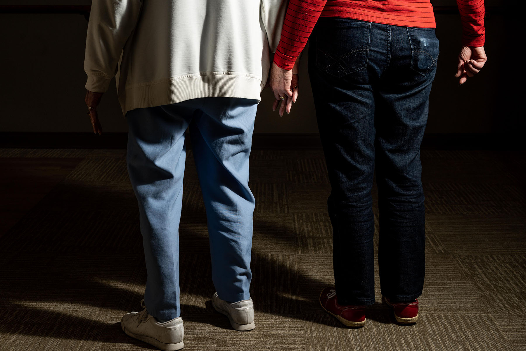 Two older women hold hands in the hallways of a community for older adults.