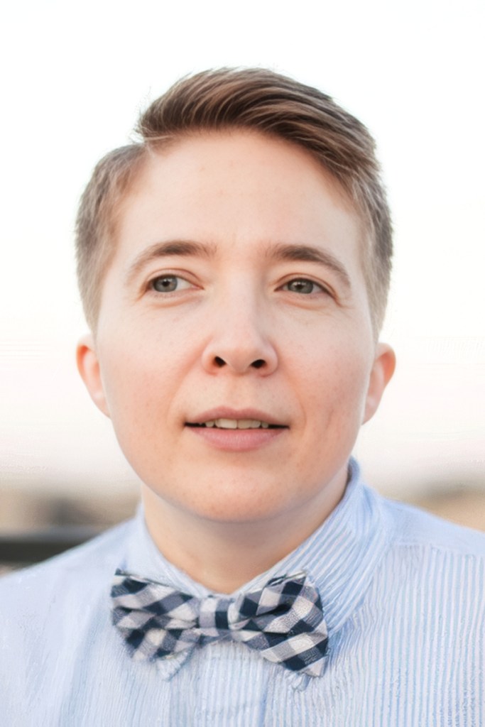 A closeup portrait of Mary wearing a collared shirt and bow tie, looking off camera.
