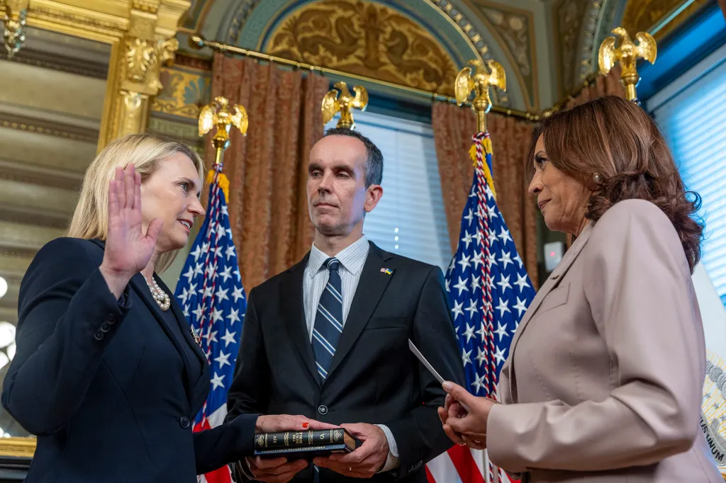 Bridget Brink raises her right hand as Kamala Harris administers the oath while Brink's husband, Nicholas Higgins, stands between them holding a book.